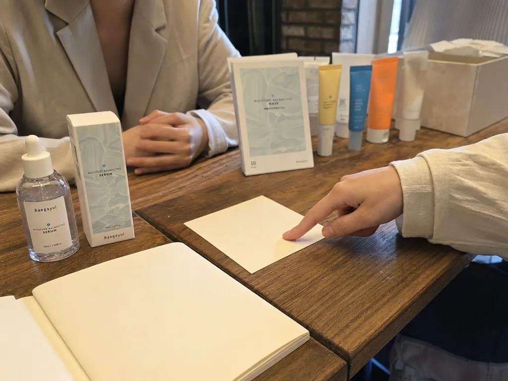 ある人物が、Baegayul製品とスキンケアチューブの横にある空白のメモカードを指差しています。